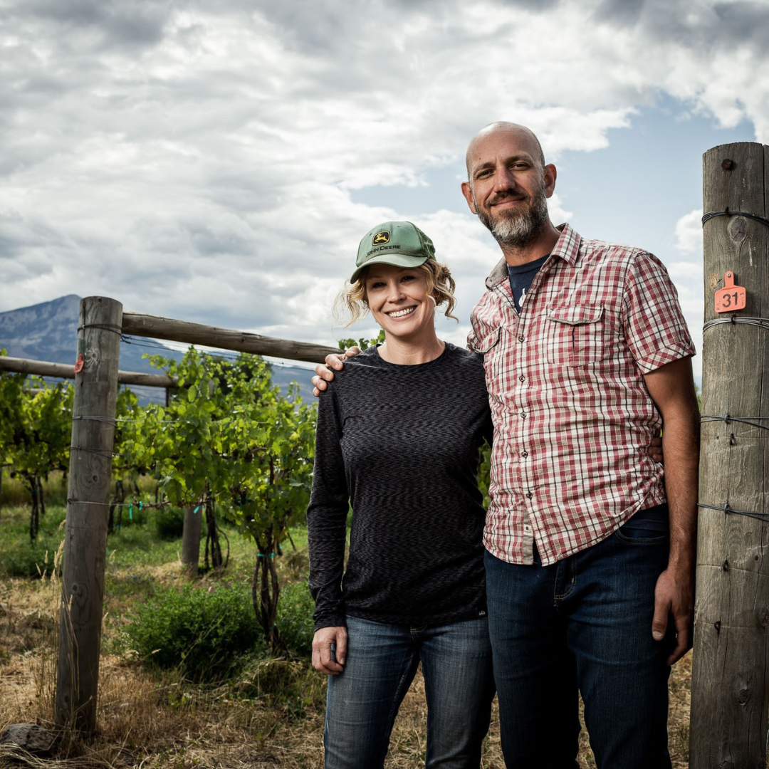 two people standing next to each other in a vineyard.