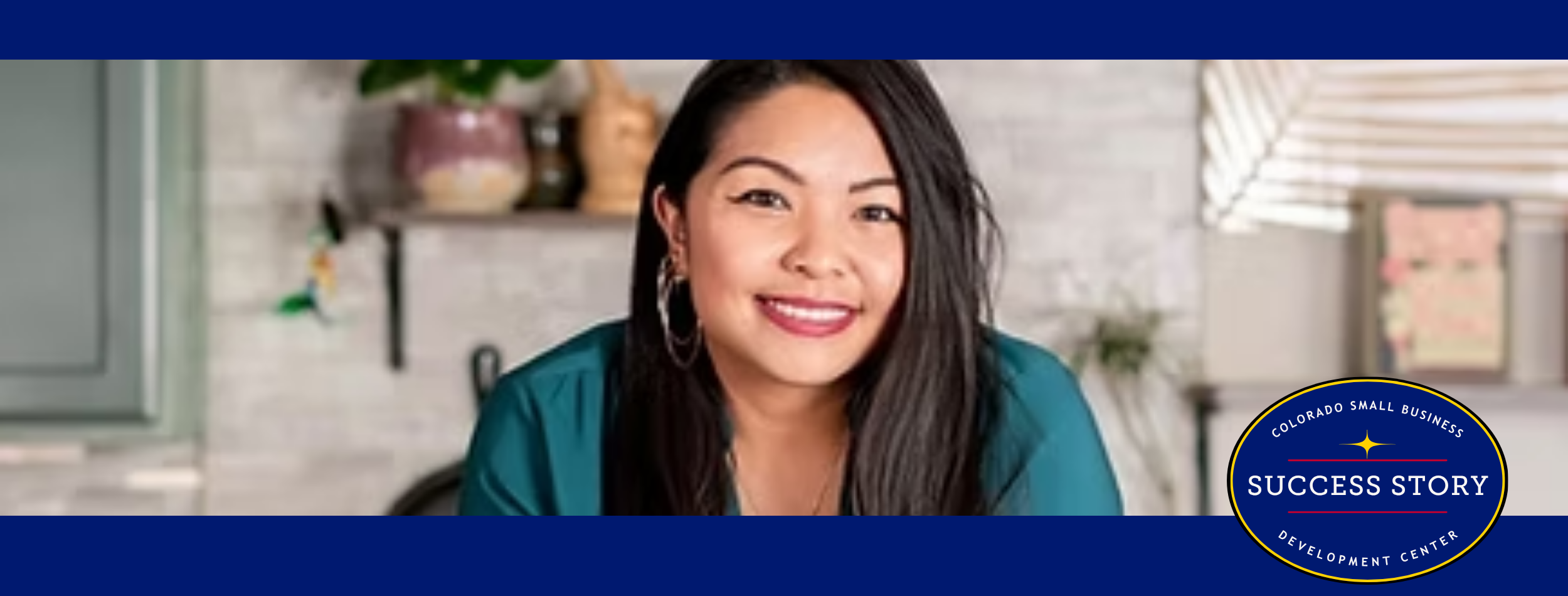 a person with long black hair sitting at a table in a kitchen.