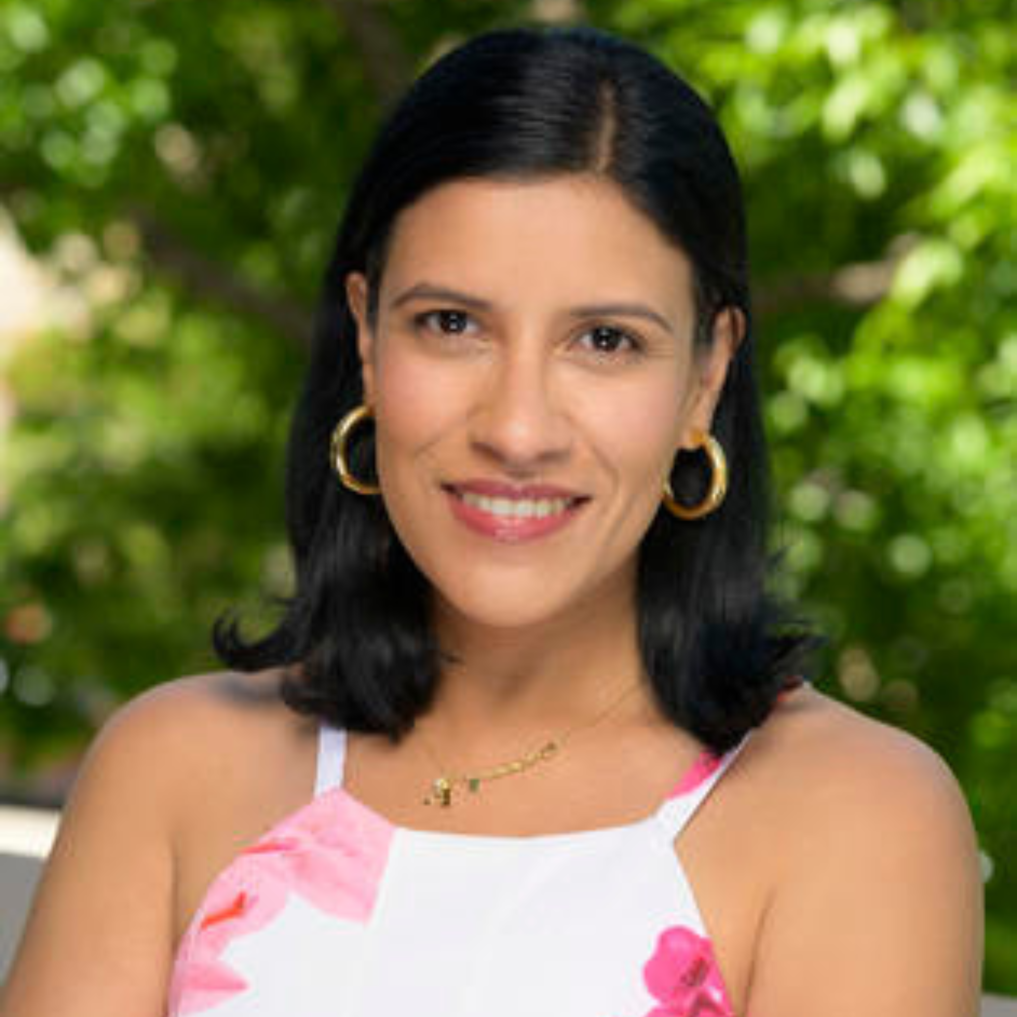 a woman in a white and pink dress standing in front of a tree on a sunny day.