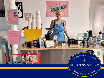 a person standing behind a business coffee counter wearing an apron and smiling.