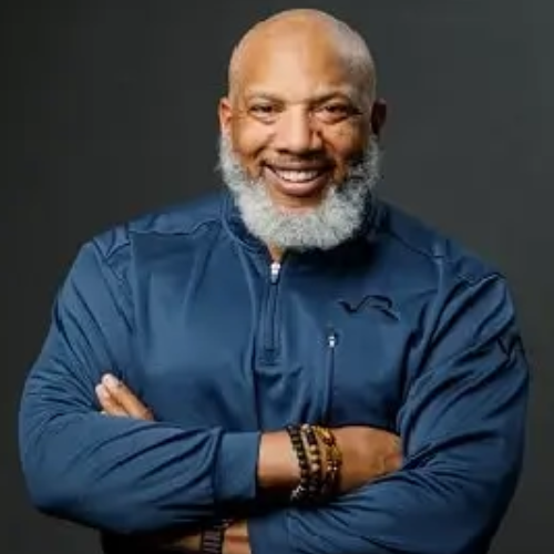 Man smiling wearing a blue shirt with crossed arms.
