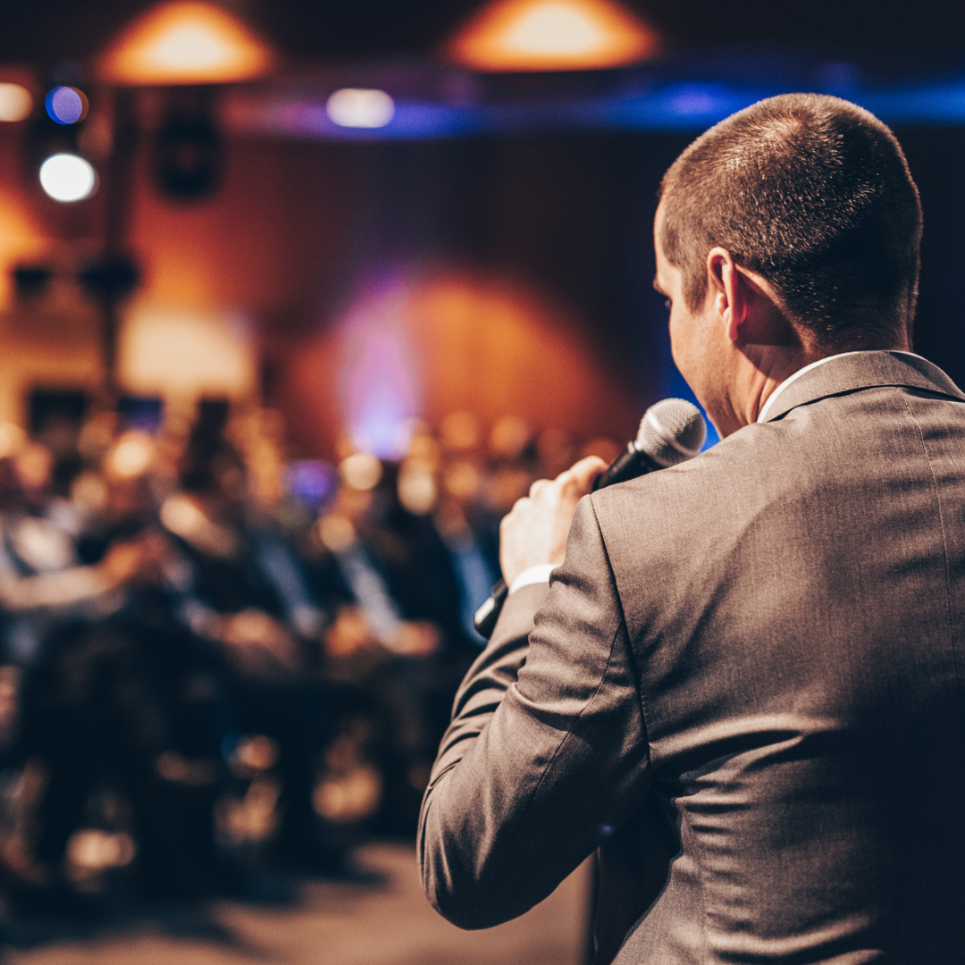 Image of a person standing in front of crowd speaking into microphone
