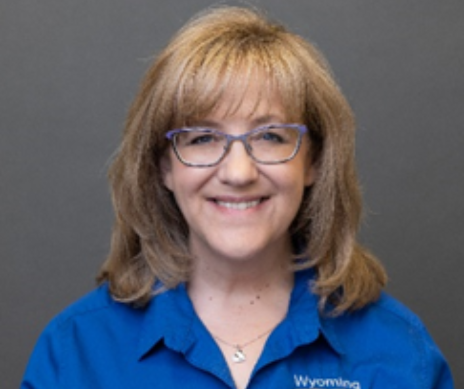 A blonde woman wearing glasses and a blue shirt smiling.