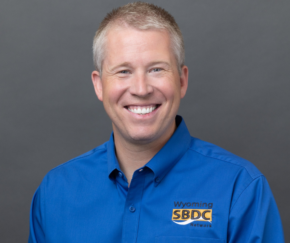 A man with grey hair wearing a blue shirt smiling.