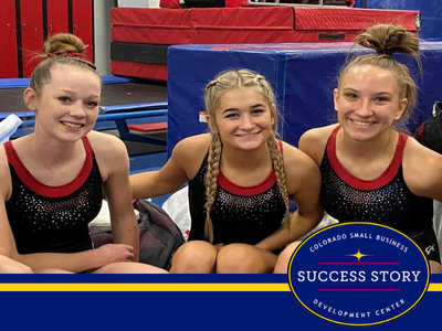 three individuals are smiling in front of a gymnastics mat.