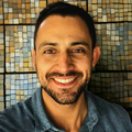 a smiling person wearing a blue shirt in front of a mosaic wall.