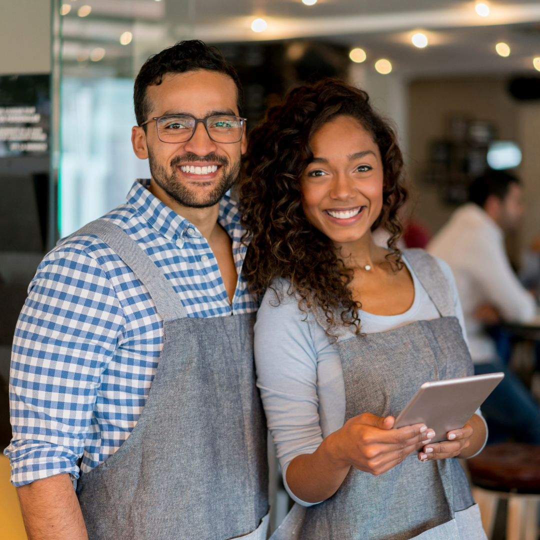 Two people in aprons standing in front of a coffee shop.