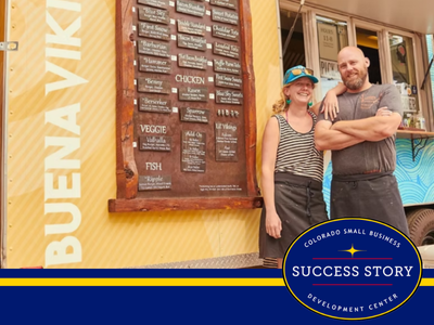 Two people standing in front of a food truck.