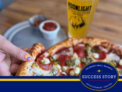 a hand holding a slice of pepperoni pizza next to a glass of beer.