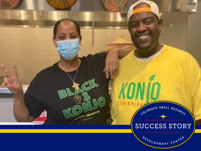 two people wearing face masks standing in front of a table with food