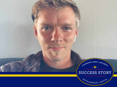 A person wearing a plaid shirt sitting on a couch looking at the camera.