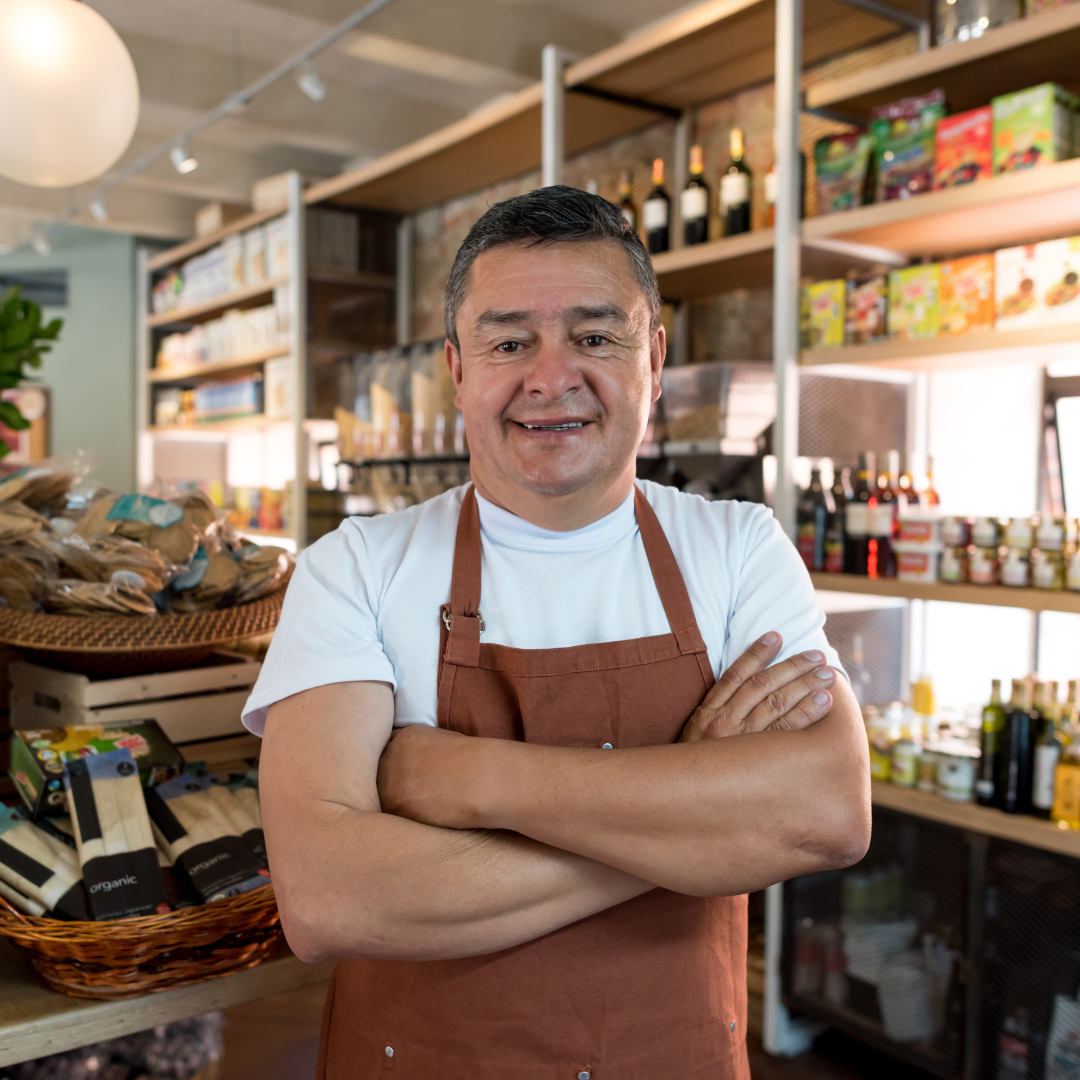 A person in an apron standing in front of shelves of food.