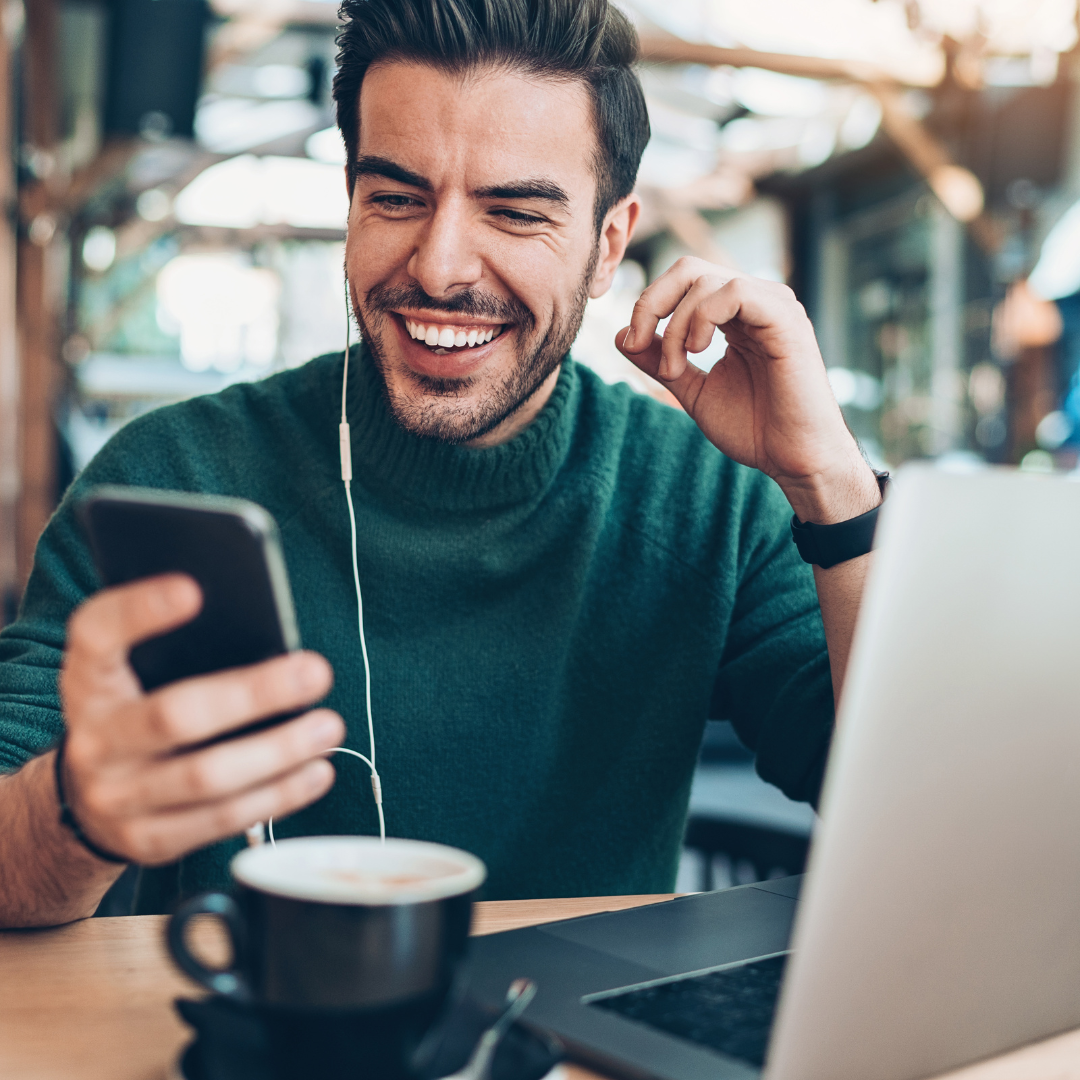 smiling person listening to music on their phone in coffee shop.