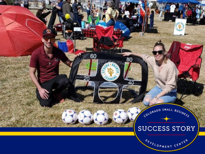 two people sitting on the grass with soccer balls.