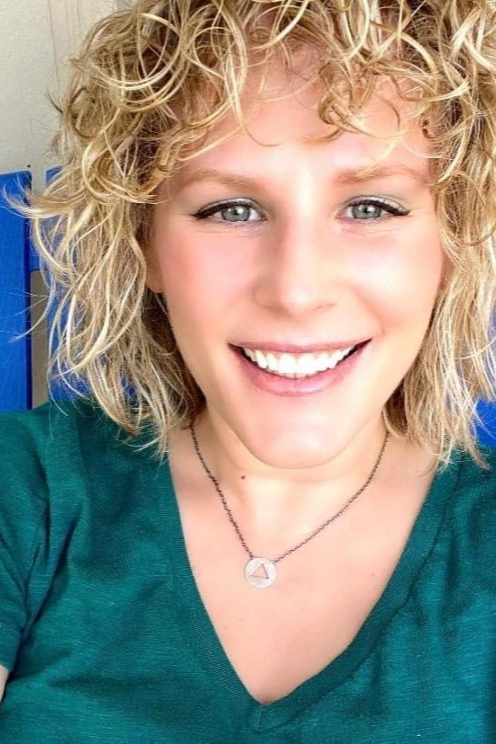 Head shot image of Nina Brandin. They are the owner of NINAB Jewelry. They have short curly hair, green eyes, and is wearing a green shirt with a necklace.  