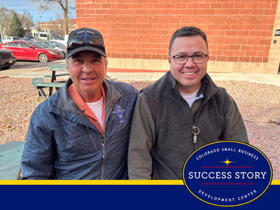 two people standing next to each other in front of a brick building
