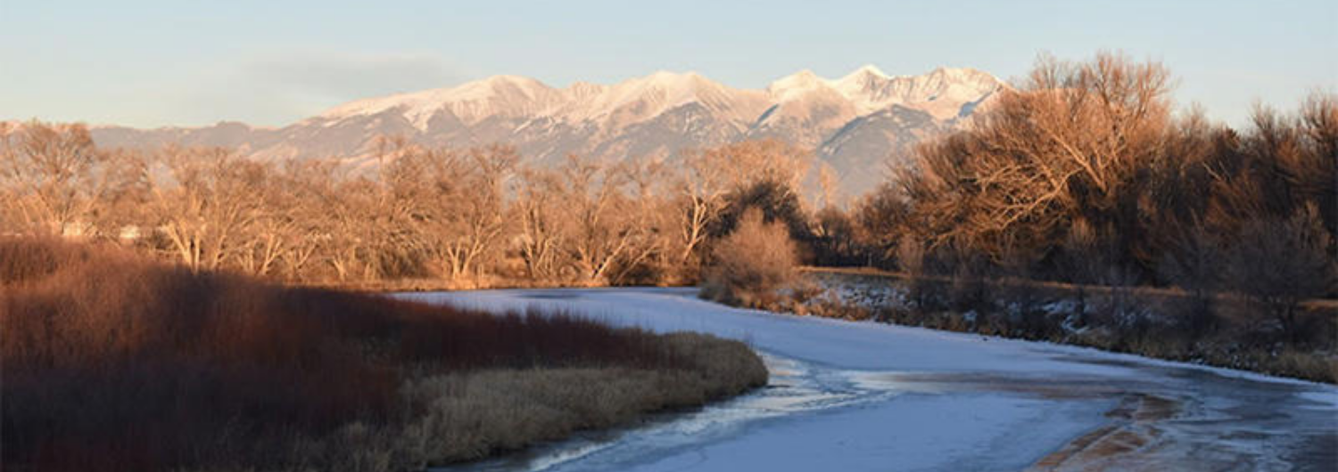 a river runs through a snowy field with mountains in the background