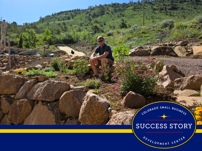 A person sitting on a rock wall with flowers.