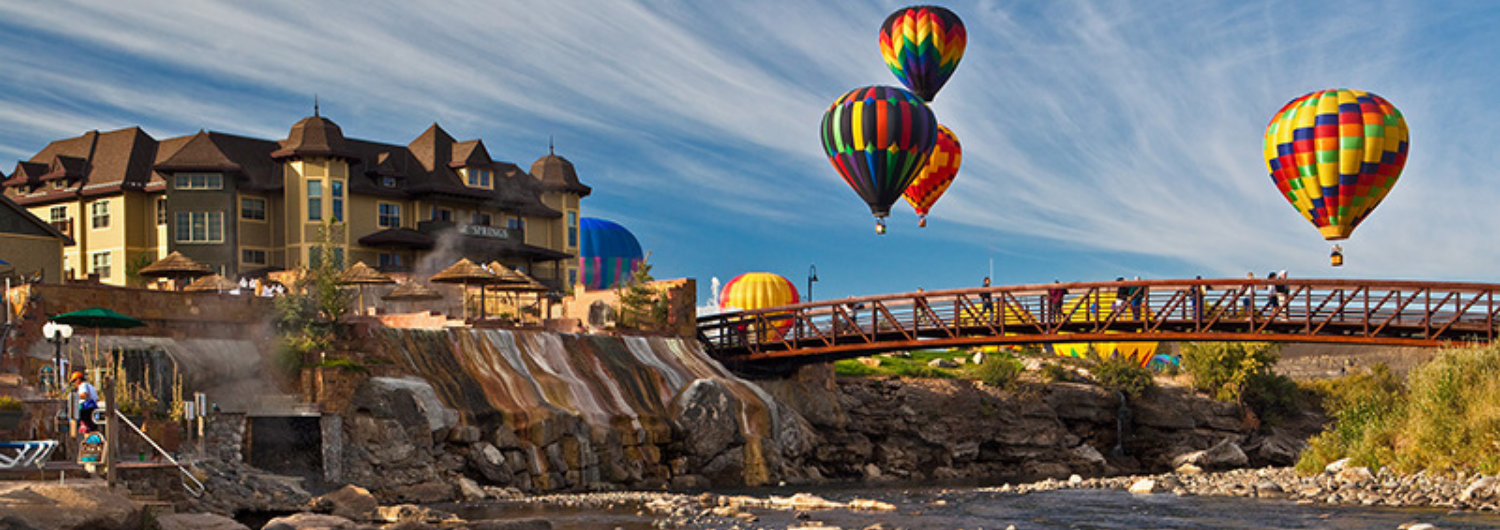 hot air balloons are flying over a bridge over a river.