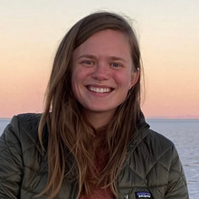A smiling person standing in front of a body of water