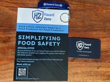 There is Hazard Zero pamphlet, business card and bottle opener. They are varying colors of white, blue, dark blue and gray.
