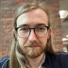A close-up of a person wearing glasses with long hair and a beard.