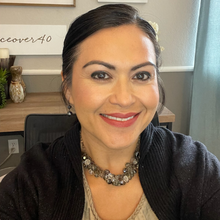 A person smiles wearing a necklace and a black sweater.