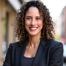 a person with curly hair wearing a suit and smiling.