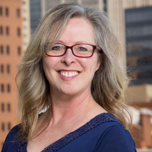 a person with glasses and a blue shirt standing in front of a city skyline.